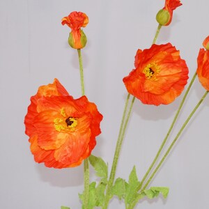 May include: Close-up of orange and yellow artificial poppy flowers with green stems and leaves. The flowers are in various stages of bloom, with some fully open and others still in bud form. The petals have a textured appearance.