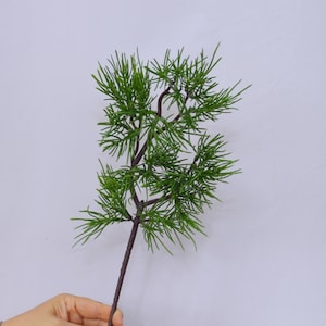 May include: A single artificial pine branch with green needles and a brown stem. The branch is about 12 inches long.