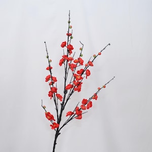 Op de afbeelding: Kunstmatige pruimenbloesemtak met felrode bloemen en groene knoppen. De donkere takken contrasteren met de heldere bloesems. Ideaal voor bloemstukken en interieurdecoratie.