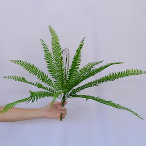Può includere: Una pianta di felce artificiale verde con più steli e foglie. La felce è disposta a forma di bouquet.