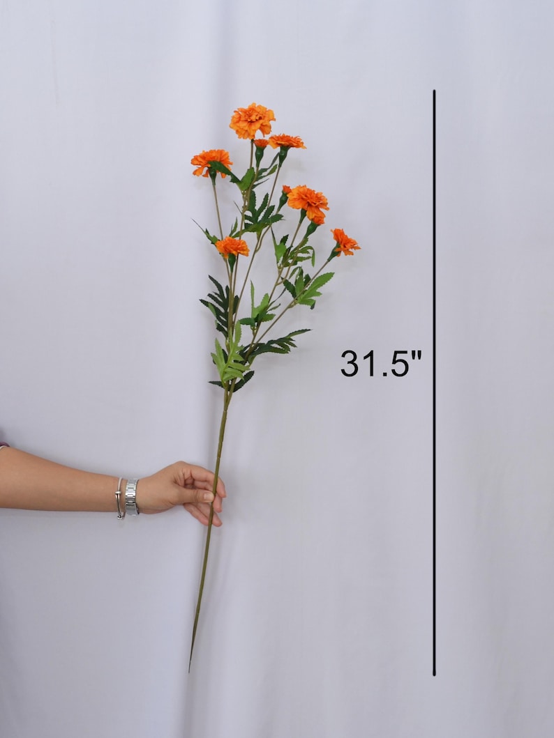 K&ouml;nnte beinhalten: Ein einzelner Stiel k&uuml;nstlicher Ringelblumen mit leuchtend orangefarbenen Bl&uuml;ten und gr&uuml;nen Bl&auml;ttern. Der Stiel ist 80 cm lang und eignet sich perfekt f&uuml;r Blumengestecke und Heimdekoration.