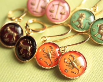 May include: Gold tone earrings with zodiac symbols. The earrings feature a variety of zodiac signs, including a scorpion, a goat, a lion, and a scale. The earrings are a great way to show your zodiac pride.