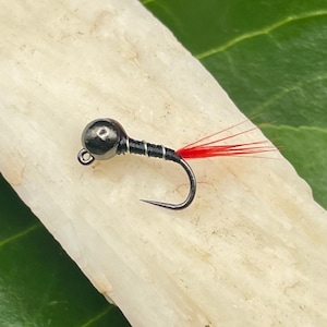 May include: A black and red fly fishing lure with a bead head and a red feather tail.