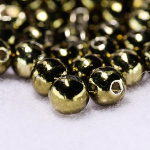 Può includere: Primo piano di un mucchio di perline rotonde dorate. Le perline sono lucide e hanno una superficie liscia.