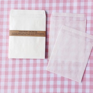 May include: Two white paper envelopes on a pink and white gingham background. The smaller envelope has a brown label with the text "CICIA IN THE SKY etsy.cicla.com Eco-friendly glassine bags made in the UK from 100% pine cellulose. Compostable & biodegradable, please dispose of it in a compost bin."