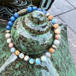 May include: A bracelet made of blue, brown, and white stones with a gold metal accent.