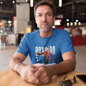 May include: A man wearing a blue t-shirt with a graphic of Cristiano Ronaldo in a soccer uniform. The graphic includes the text "RONALDO" and the number "7".