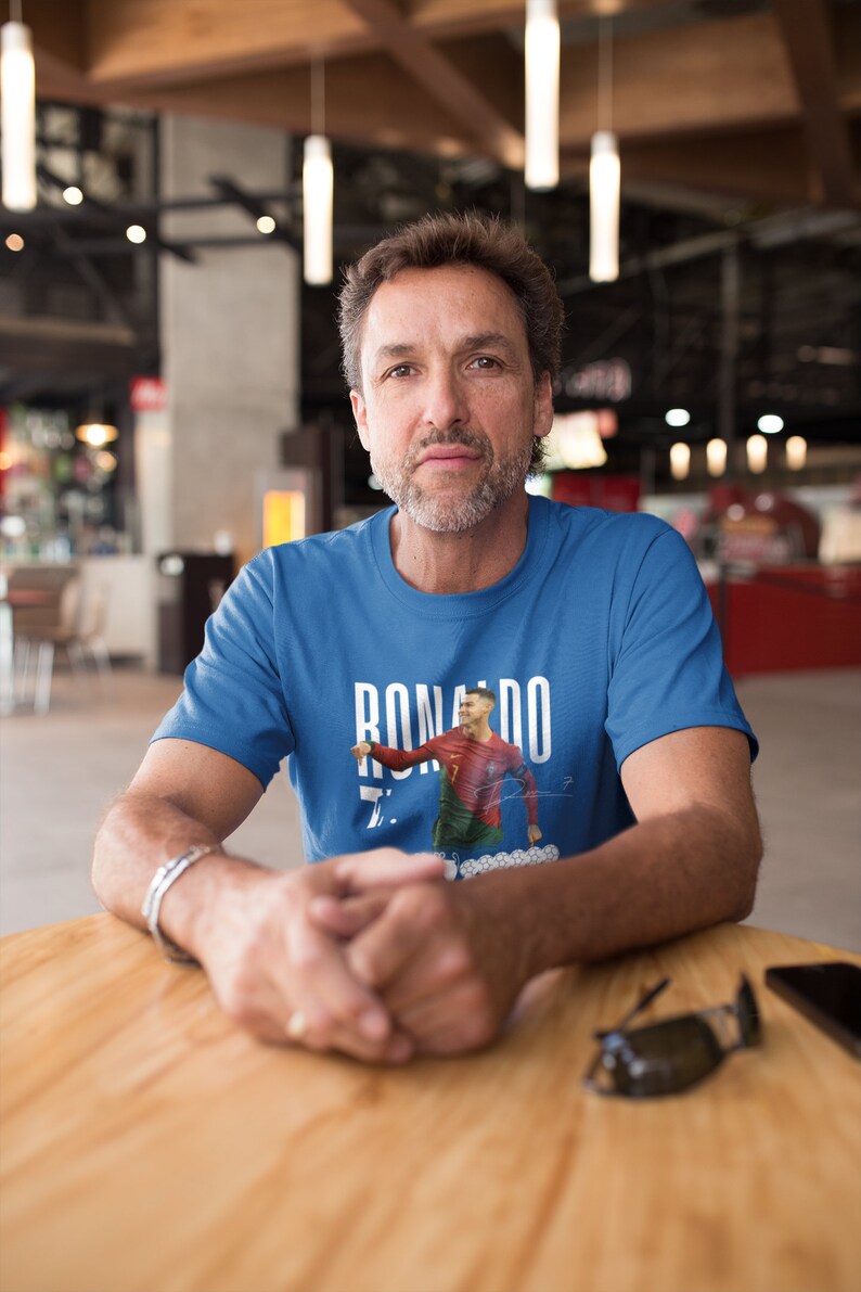 May include: A man wearing a blue t-shirt with a graphic of Cristiano Ronaldo in a soccer uniform. The graphic includes the text "RONALDO" and the number "7".