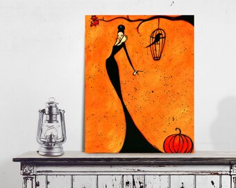 Puede incluir: Una impresión artística naranja y negra que presenta a una mujer con un vestido largo negro, un pájaro en una jaula y una calabaza. La obra de arte se exhibe en un gabinete blanco desgastado con una linterna plateada y un maniquí.
