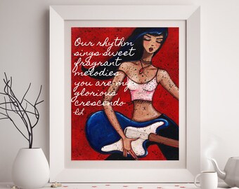 Puede incluir: Impresión artística enmarcada que muestra a una mujer tocando una guitarra eléctrica azul sobre un fondo rojo. La obra de arte incluye el texto "Our rhythm sings sweet fragrant melodies, you are my glorious crescendo." La mujer lleva un top rosa y pantalones oscuros.