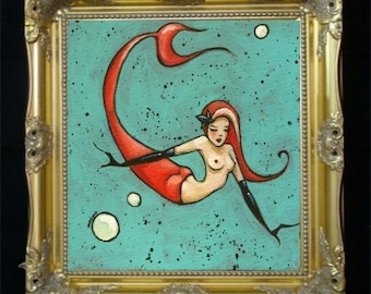 Puede incluir: Pintura enmarcada de una sirena con cabello rojo y cola roja, nadando en un fondo turquesa con burbujas. La sirena lleva guantes negros y un accesorio para el cabello negro. El marco es dorado y ornamentado.