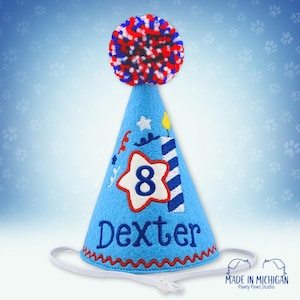 May include: Blue felt party hat with a red, white, and blue pom-pom on top. The hat has a white star with the number 8 in the center, a striped candle, and the name Dexter embroidered on it.