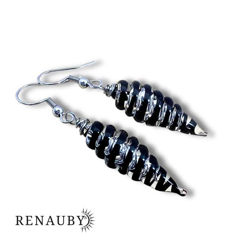 May include: A pair of black and silver spiral earrings. The earrings have a silver hook and are made of black glass beads. The earrings are in a spiral shape and are hanging on a white background. The brand name "RENAUBY" is at the bottom.
