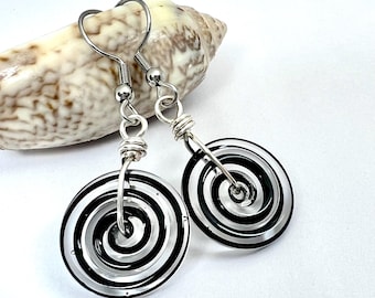 May include: A pair of spiral design earrings. Each earring has a black and white spiral pattern within a clear, circular frame. The earrings are suspended from silver-coloured hooks.