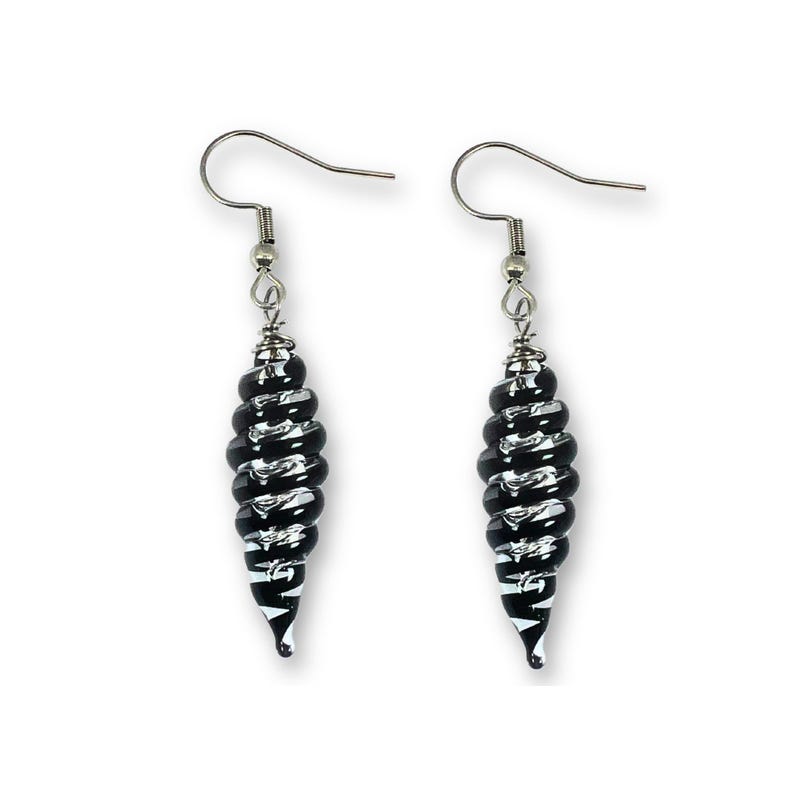 May include: A pair of dangle earrings with a black and white spiral design. The earrings have a silver-colored hook and a decorative spiral-shaped bead. The beads are black with white stripes, creating a contrasting pattern.