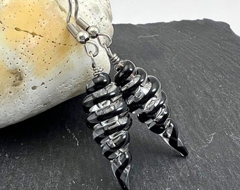 May include: Spiral earrings featuring alternating black and clear glass sections. The earrings are suspended from silver-coloured ear wires. The design is elegant and striking, suitable for various occasions. The earrings are displayed against a neutral background.