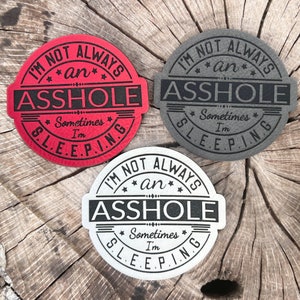 May include: Three round coasters with a black and white design. The coasters feature the text "I'm not always an asshole, sometimes I'm sleeping." The coasters are red, grey, and white.