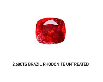 Puede incluir: Una vibrante gema de rodonita roja con talla cojín. La gema es de Brasil y pesa 2,68 quilates. El texto debajo de la gema dice: 2.68CTS BRAZIL RHODONITE UNTREATED.