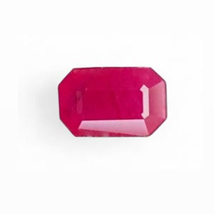 May include: A faceted, rectangular-cut ruby gemstone. The gem is a deep, vibrant red color with a polished surface. The shape is an emerald cut, with a series of rectangular facets. The gemstone is set against a white background.