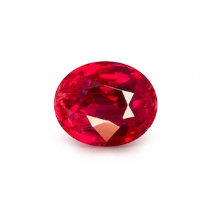 Puede incluir: Una gema roja de corte ovalado con una superficie facetada que refleja la luz. La piedra muestra un tono carmesí profundo y saturado en toda su estructura, exhibiendo cortes geométricos precisos que crean patrones de luz interna.