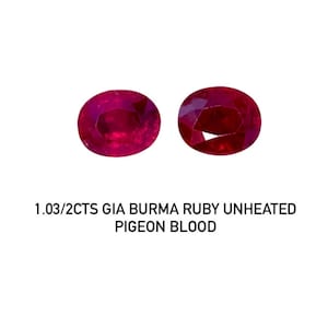 May include: Two oval-cut, unheated Burma rubies with a deep red hue, displayed against a white background. The text below reads: "1.03/2CTS GIA BURMA RUBY UNHEATED PIGEON BLOOD."