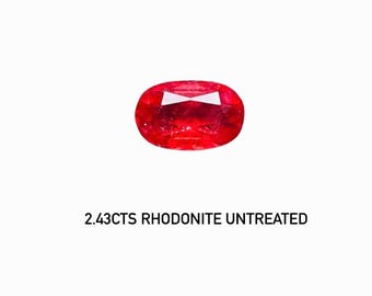 May include: A vibrant red, oval-shaped rhodonite gemstone. The gem is untreated and has a weight of 2.43 carats. The stone is set against a white background, highlighting its color and clarity.