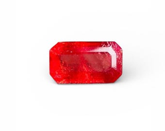 May include: A vibrant, rectangular-cut ruby gemstone. The gem is a deep, saturated red color with a faceted surface, set against a clean white background. The shape is an elongated rectangle with cut corners, showcasing its clarity and brilliance.