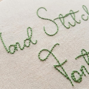 Puede incluir: Primer plano de un lienzo con texto bordado en verde. Las palabras "land Stitch" y "of for" son visibles, mostrando un diseño de bordado hecho a mano. La costura es detallada y el color es un verde vibrante.