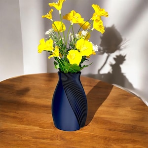 May include: A dark blue vase with a wavy, textured design holds a bouquet of yellow flowers. The vase is sitting on a wooden table.