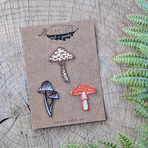 Könnte beinhalten: Set mit drei Bügelbildern von Pilzen. Die Bügelbilder sind braun, weiß und orange. Die Bügelbilder befinden sich auf einer braunen Karte mit dem Text "likesara art + goods www.likesara.com iron-on patch set".