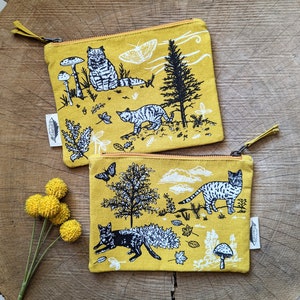 May include: Two yellow fabric pouches with black and white illustrations of cats, mushrooms, trees, and butterflies. The pouches have zipper closures and are lined with a yellow fabric.