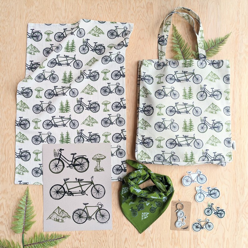 Pu&ograve; includere: Un set di quattro articoli con un design a tema bicicletta. Il set include una borsa di tela verde e bianca, un asciugamano da cucina verde e bianco, una bandana verde e un set di quattro adesivi per bicicletta verde e bianco. La borsa di tela ha uno sfondo bianco con biciclette verdi e foglie verdi. L'asciugamano da cucina ha uno sfondo bianco con biciclette verdi e foglie verdi. La bandana ha uno sfondo verde con biciclette bianche e foglie bianche. Gli adesivi hanno uno sfondo bianco con biciclette verdi e foglie verdi.