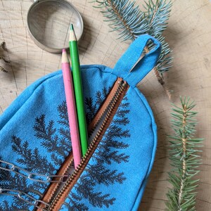Pu&ograve; includere: Un astuccio in tela blu brillante con stampa di foglie di felce nere e chiusura a zip marrone. L'astuccio &egrave; dotato di un passante in tessuto e contiene una matita rosa, una matita verde e una catena di graffette in metallo argentato.