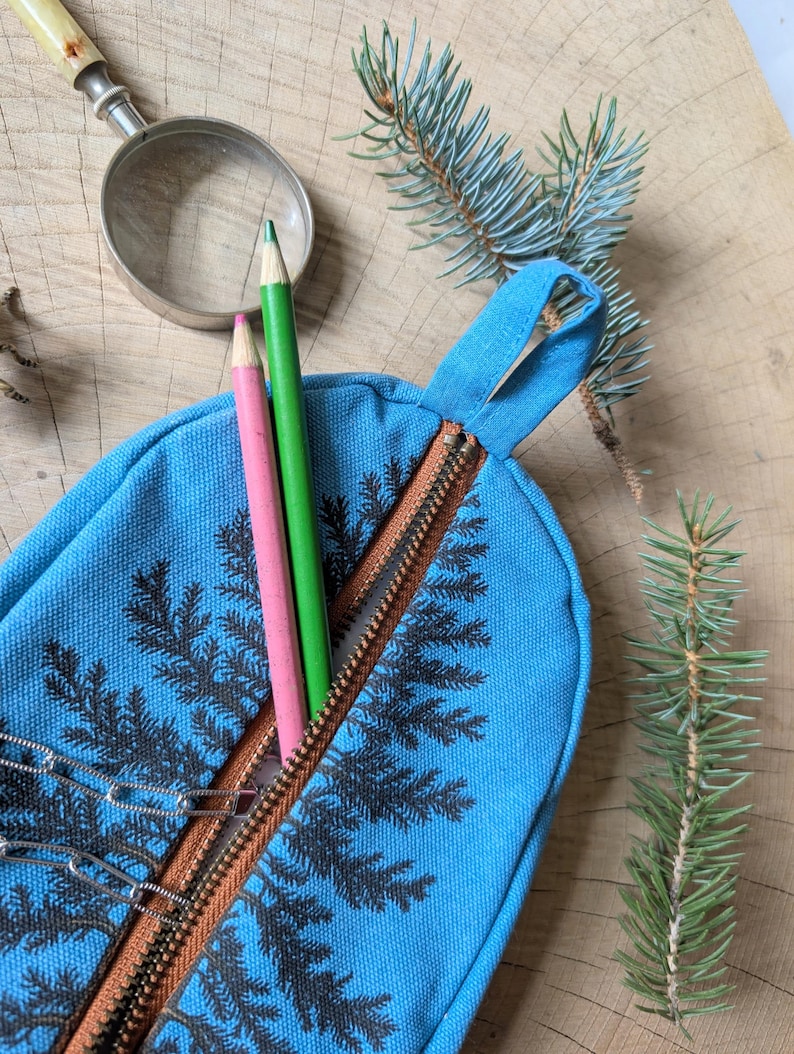 Pu&ograve; includere: Un astuccio in tela blu brillante con stampa di foglie di felce nere e chiusura a zip marrone. L'astuccio &egrave; dotato di un passante in tessuto e contiene una matita rosa, una matita verde e una catena di graffette in metallo argentato.