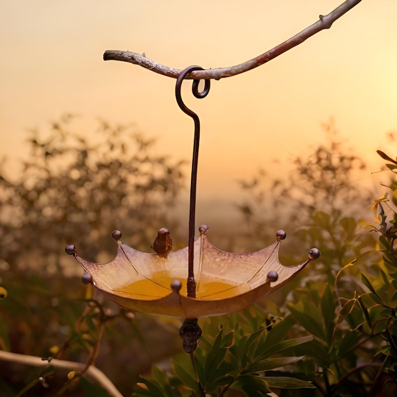 May include: A metal bird feeder shaped like an umbrella with a brown stem and a yellow, gold, and brown umbrella top. The feeder is hanging from a branch with a brown stem.