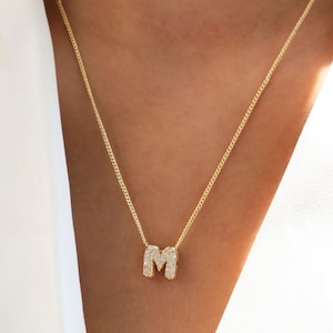 Op de afbeelding: Een gouden ketting met een letter M hanger ingelegd met kleine heldere stenen.