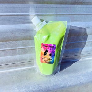 May include: A clear plastic pouch filled with bright green powder. The pouch has a white spout and a colorful label that reads "Break Dust" with a graphic of two dogs. The label also states "Non-Toxic Fun Colorful Break".