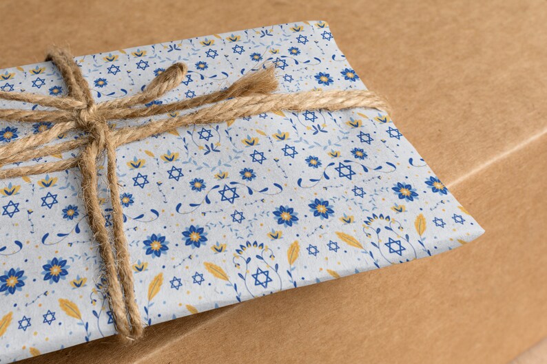 K&ouml;nnte beinhalten: Ein Geschenk, das in wei&szlig;es Papier mit einem blauen und gelben Blumenmuster mit Davidsternen eingewickelt ist. Das Geschenk ist mit braunem Garn gebunden.