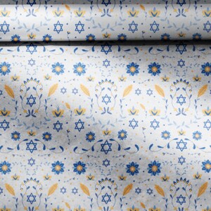 K&ouml;nnte beinhalten: Wei&szlig;es Geschenkpapier mit einem sich wiederholenden Muster aus blauen Blumen, gelben Bl&auml;ttern und blauen Davidsternen.