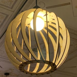 May include: A spherical pendant light fitting constructed from light-coloured wooden slats arranged in a curved, open-frame design. A single glowing white light bulb is positioned in the centre, casting light through the gaps between the wooden pieces.