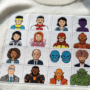 Op de afbeelding: Crèmekleurige trui met een vierkante geborduurde patch. De patch toont een raster van kleurrijke cartoonfiguren, elk met een uniek superhelden-achtig kostuum. De patch is gecentreerd op de trui.