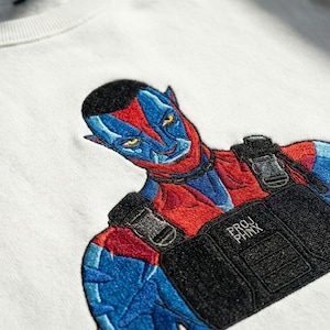 May include: A white crewneck sweatshirt featuring a detailed embroidered graphic of a blue and red humanoid character with pointed ears. The character wears a black tactical vest with the text PROJ PHNX embroidered in white on the front chest area.