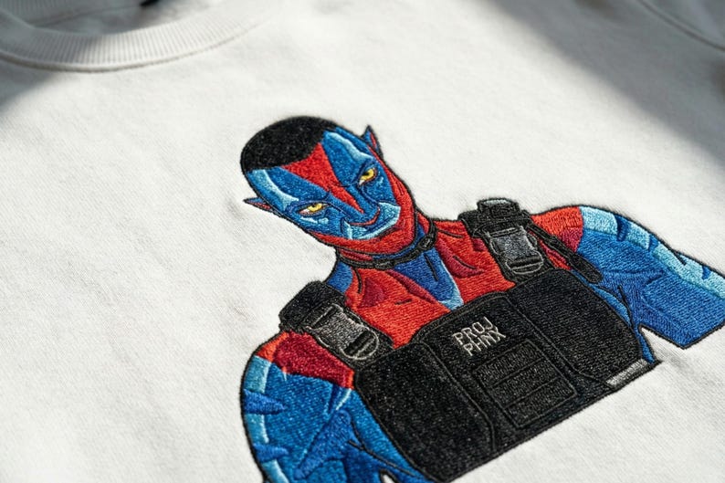 May include: A white crewneck sweatshirt featuring a detailed embroidered graphic of a blue and red humanoid character with pointed ears. The character wears a black tactical vest with the text PROJ PHNX embroidered in white on the front chest area.