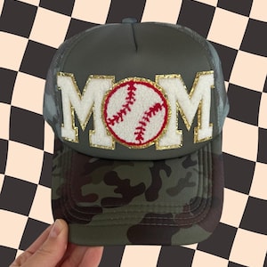 May include: A green camouflage trucker hat with a white and gold MOM patch and a red and white baseball graphic.