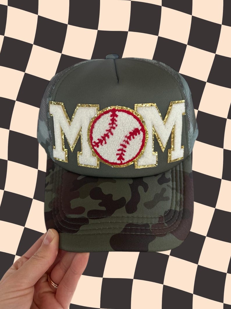 May include: A green camouflage trucker hat with a white and gold MOM patch and a red and white baseball graphic.