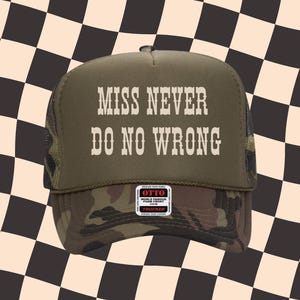 May include: Olive green and camouflage trucker hat with the text "MISS NEVER DO NO WRONG" in white block letters. The hat features a mesh back and a curved brim. A small Otto brand tag is visible.