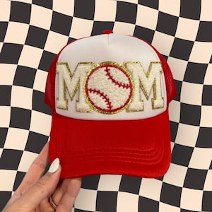 May include: A red and white trucker hat with a gold glitter MOM patch and a white baseball with red stitching in the center.