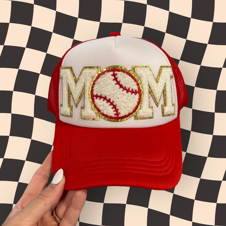 May include: A red and white trucker hat with a gold glitter MOM patch and a white baseball with red stitching in the center.