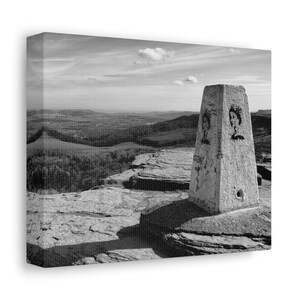 May include: A black and white photograph of a stone marker on a mountaintop. The marker is a tall, rectangular stone with a flat top. The marker is inscribed with the number "2". The marker is surrounded by rocks and a view of a valley in the distance.
