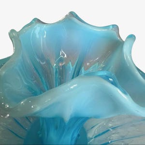 Puede incluir: Primer plano de un cuenco decorativo de cristal azul claro. El cuenco tiene una forma org&aacute;nica &uacute;nica con bordes fluidos en forma de p&eacute;talo. El cristal tiene un acabado brillante, que refleja la luz y crea una sensaci&oacute;n de profundidad y movimiento. Es un art&iacute;culo decorativo.